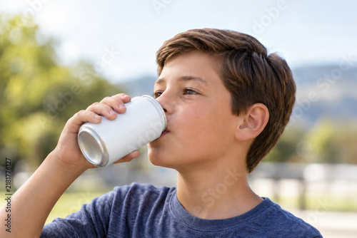 Close up of boy drinking from a blank white aluminum can outdoors. Image with copy space.