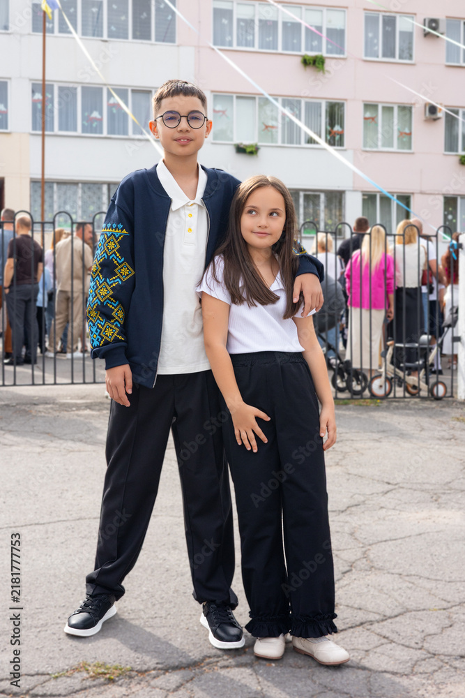 Fototapeta premium A boy and a girl pose together outdoors, dressed in smart casual attire, exuding a playful and cheerful mood.