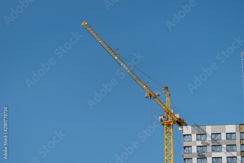 Tall yellow construction crane reaching into a clear blue sky near a modern building under development in the bustling city