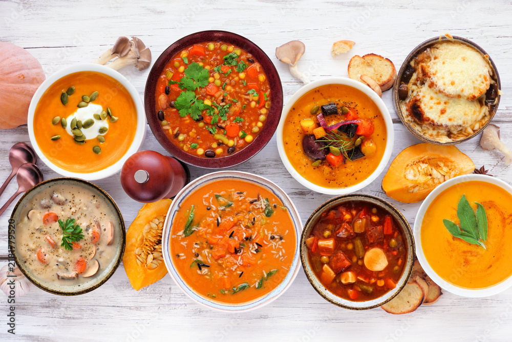 Obraz premium Selection of delicious homemade warm and cozy autumn soups. Above view table scene on a white wood background. Pumpkin, squash, sweet potato, mushroom, French onion and hearty vegetable.