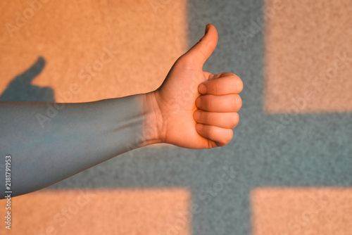 Obraz na płótnie Arm Holding Thumbs Up In Warm Light Against Textured Wall With Long Shadow Across Corner