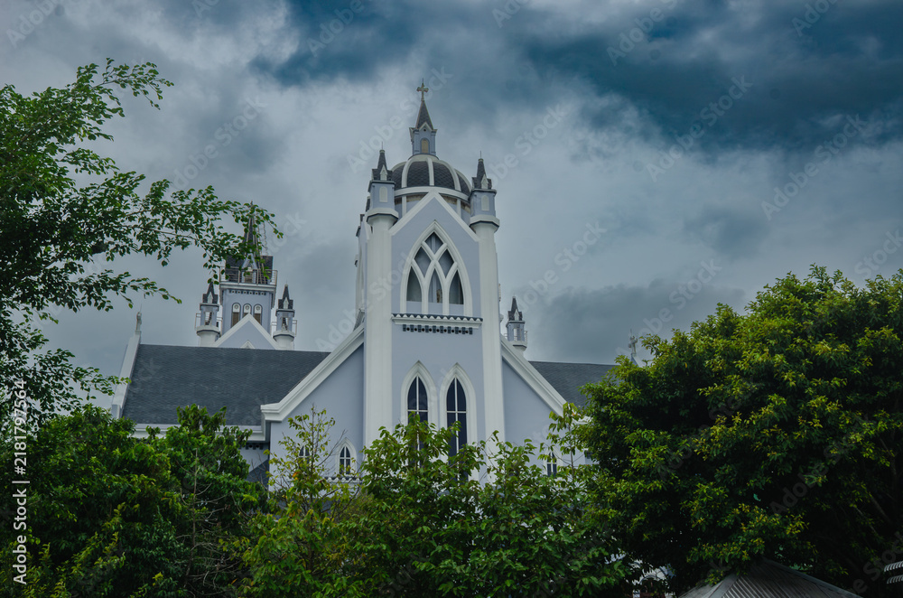 Obraz premium Roman Catholic Gothic Church with Tall Steeple and Arched Windows Under Stormy Sky