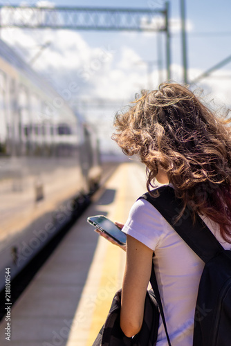 Teenage girl texts her sister on smartphone while standing alone on railway platform. Concept of digital connection and staying in touch after teen sibling train departure.