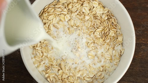Pouring milk in bowl with Oat flakes, close up. Healthy breakfast concept
