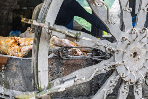 Whole Lamb Roasting on Traditional Spit Behind Rustic Wagon Wheel at Outdoor Food Event