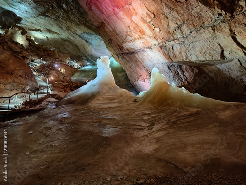 Foto Luminous underground cave with vibrant red and blue lighting showcasing stunning mineral formations like cascading stalagmites, reflective wet ground, and safety railings for visitors
