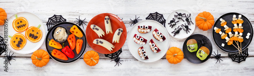 Healthy Halloween fruit and vegetable snacks. Variety of fun, spooky treats. Overhead view table scene over a white wood banner background.
