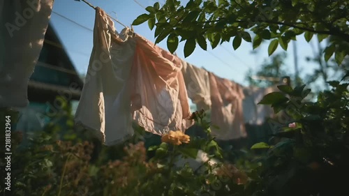 Summer hot vibe lifestyle. A candid photograph captures a serene outdoor scene during the golden hour. A line of white and peachcolored laundry hangs on a clothesline, surrounded by lush greenery.