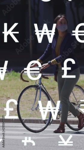 Animation of global currency symbols over asian woman in face mask wheeling bike in street