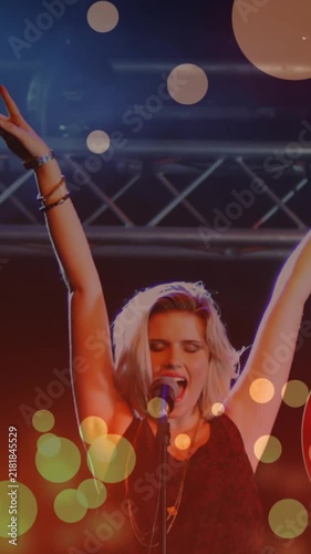 Animation of glowing spots falling over caucasian female singer holding a guitar singing at concert
