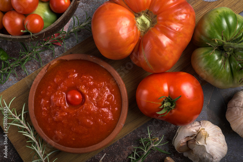 Fresh heirloom tomatoes, cherry tomatoes, garlic, green peppers, bread, and tomato sauce on a rustic wooden table with olive oil