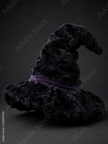 A detailed black wizard hat with a purple ribbon against a dark background ai generated
