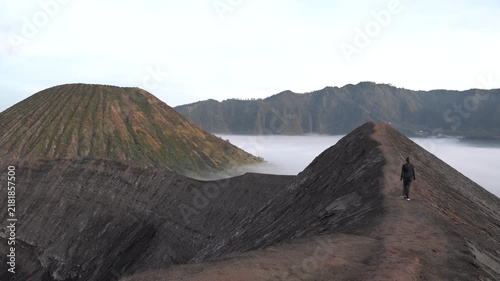 Solitary traveler walking on the edge of a volcano crater with a stunning misty mountain landscape