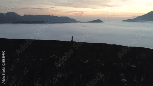 Silhouette of a lonely person hiking on a mountain peak above a sea of fog during a scenic sunrise