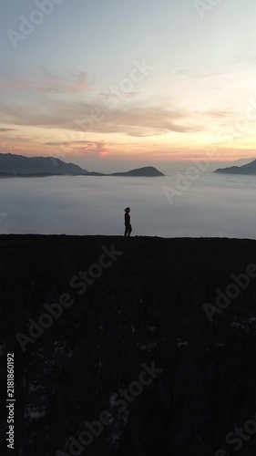 Lone person walking along a mountain summit over a stunning sea of clouds at sunrise