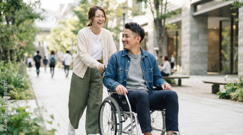Plakat 車椅子を押しながら街を笑顔で散歩する若い夫婦