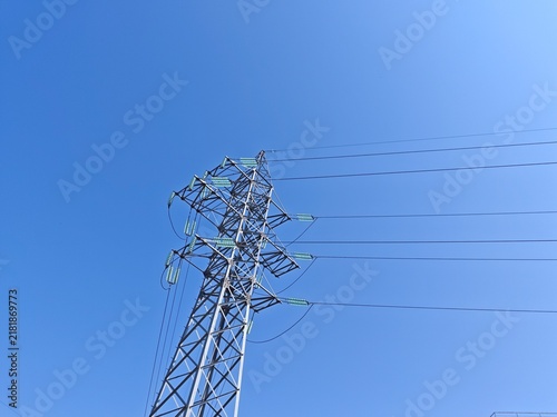 High voltage power transmission pylon with electrical wires against a clear blue sky.