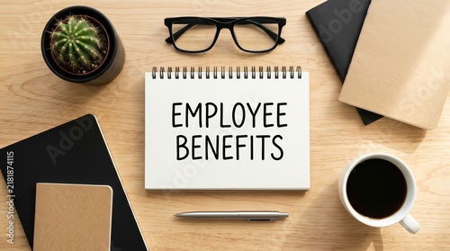Handwritten employee benefits text on a spiral notepad in a workspace setting.