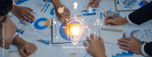 Obraz na plátně A dynamic business strategy session underway with team members discussing ideas and reviewing charts while a light bulb symbolizing innovation shines at the center