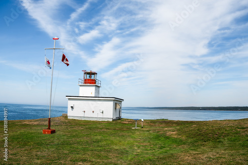 Bild auf Leinwand Small white and red lighthouse on Brier Island, Nova Scotia, featuring the Canadian flag and a sweeping view of the ocean under a blue sky