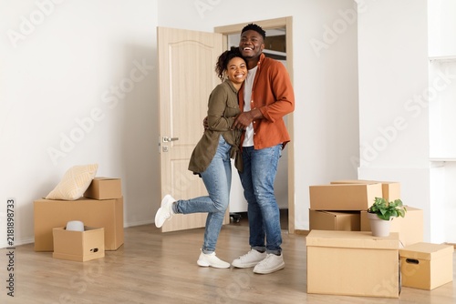 Cuadro en lienzo Happy Young African American Couple Smiling And Embracing While Moving Into New Home, Surrounded By Boxes