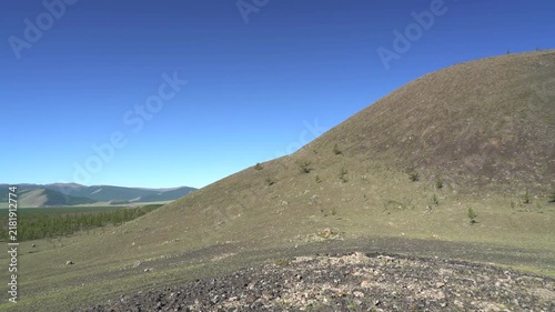 Lava tumulus forms rounded hill beside basalt plain through ancient volcanic uplift. Solidified crust swell shows non eruptive geology, rugged barren terrain, remote relief.