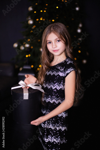 Elegant Little Girl in a Black Sequin Dress Holding a Large Round Gift Box at Christmas