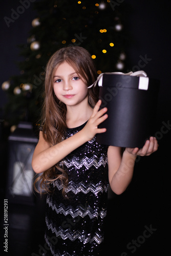 Elegant Little Girl in a Black Sequin Dress Holding a Large Round Gift Box at Christmas