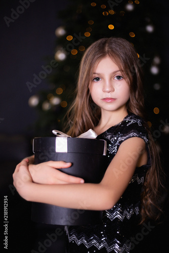 Elegant Little Girl in a Black Sequin Dress Holding a Large Round Gift Box at Christmas