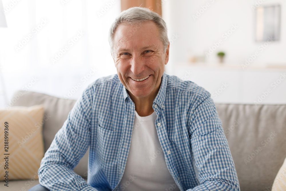 © Prostock-studio - Smiling Elderly Caucasian Man Enjoying Moment At Home, Sitting On Couch With Positive Emotion, Reflecting Joy And Happiness In Cozy Living Room Environment. Lifestyle Concept.