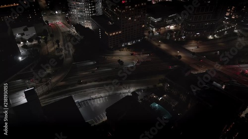 In downtown Los Angeles, California, cars and trucks are shown driving on the busy highway at night, viewed from an approaching aerial perspective.