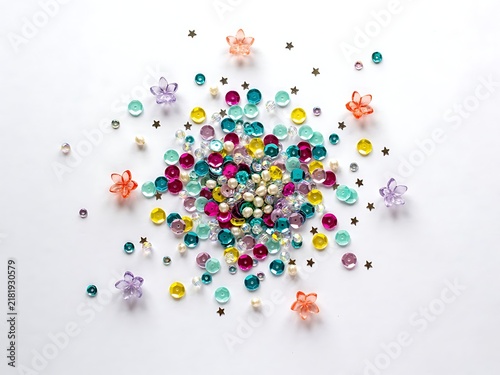 A colorful pile of glittering sequins beads and decorative flower shaped elements on a white background