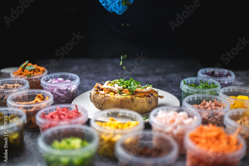 Baked potatoes with cheese, herbs, meat and butter. Copy space background. BBQ or steakhouse side dish favorite with tomato beans, cheddar cheese, bacon.