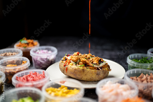Baked potatoes with cheese, herbs, meat and butter. Copy space background. BBQ or steakhouse side dish favorite with tomato beans, cheddar cheese, bacon.