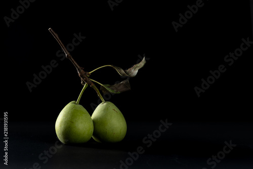 Cuadro en lienzo Two green pears with branch on black background, dramatic chiaroscuro lighting –