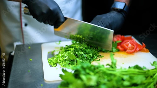 A professional chef is chopping coriander on a chopping board. 4K close up view of fresh coriander and tomato.