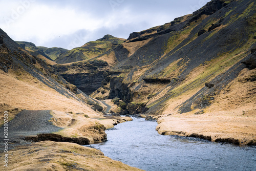 Kvernuholsa River flowing from a gorge of rocks and yellowed grass in Iceland in the Skogar area during a cloudy day