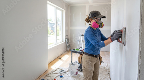 Worker wearing respirator mask diligently sands freshly installed drywall seams inside a new home