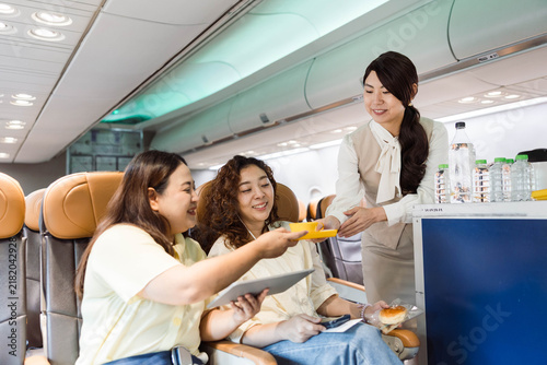 Foto Flight attendant serves meals and drinks to two smiling passengers in an airplane cabin, highlighting inflight hospitality, comfort, and friendly service during air travel