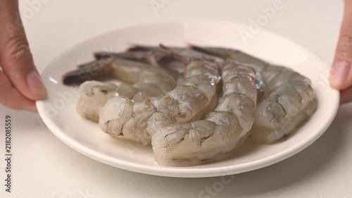 Slow motion of hand rotating fresh Pacific white shrimp on white plate, raw seafood ingredient