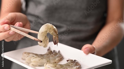 Hand using chopsticks to pick up fresh Pacific white shrimp from a white plate to show raw seafood ingredient