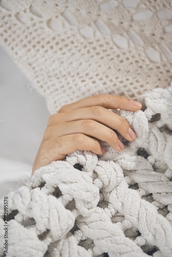 Hand is gently holding soft blanket while resting on comfortable bed at home during evening time. The setting shows a warm and inviting feeling with textiles around