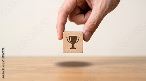Hand holding wooden block with trophy icon symbolizing success, achievement, winning business goal, career victory, award, leadership, first place prize, motivation, excellence
