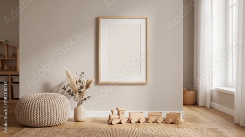 Minimalist nursery room interior with empty vertical poster frame mockup on beige wall, wooden toy train and knitted pouf on floor, scandi style kids bedroom decoration