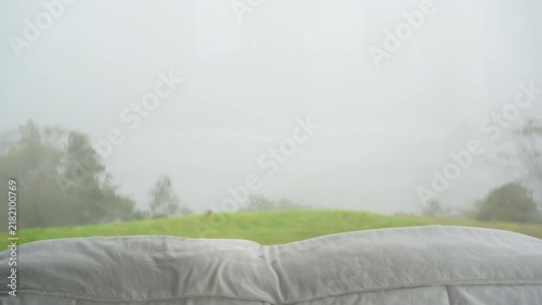 View of Phu Thap Boek garden home resort in bedroom with white pillow blanket on bed and rain dew on glass wall window on high hill mountain in green lawn garden with fog mist clouds sky in Thailand