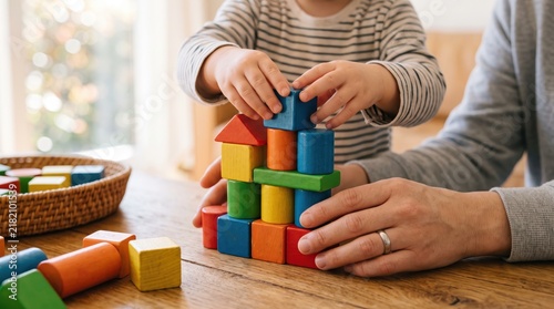 Toddler child playing with colorful wooden building blocks, stacking tower with parent assistance, early childhood education and development, fine motor skills learning activity