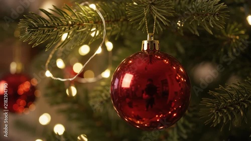 Beautifully decorated Christmas tree featuring red and gold ornaments with glowing warm string lights in a cozy indoor living room setting near a fireplace.