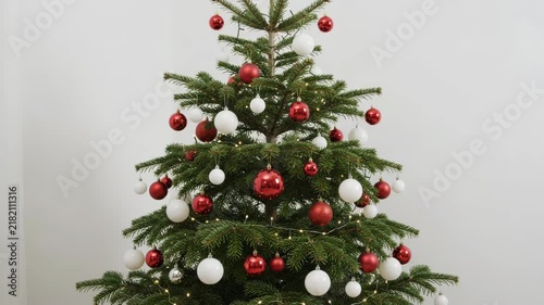 Beautifully decorated Christmas tree featuring red and white ornaments with glowing fairy lights against a minimalist white background, perfect for festive holiday celebrations.