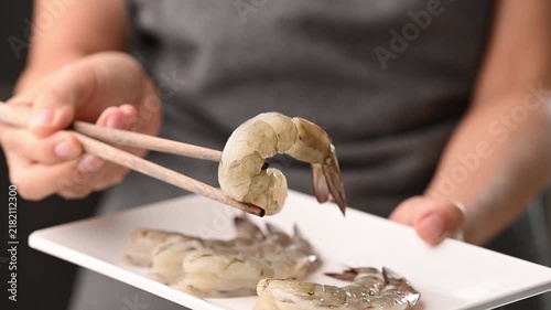 Hand using chopsticks to pick up fresh Pacific white shrimp from a white plate to show raw seafood ingredient