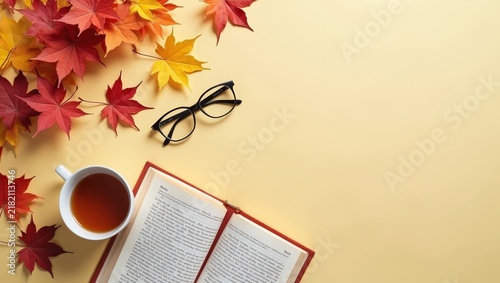Cozy autumn flat lay with an open book, cup of tea, reading glasses and colorful maple leaves. Warm seasonal composition creating a peaceful atmosphere for relaxation, reading and fall lifestyle.